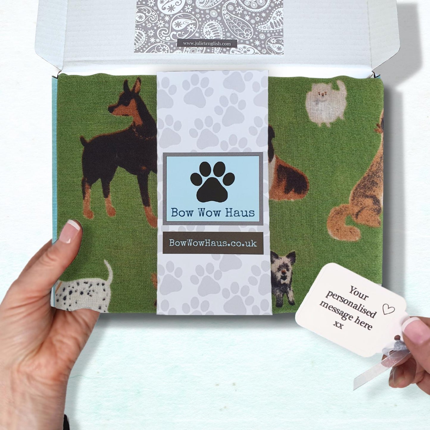 dog-themed scarf in a box with a personalized message tag held by a hand on a white background.