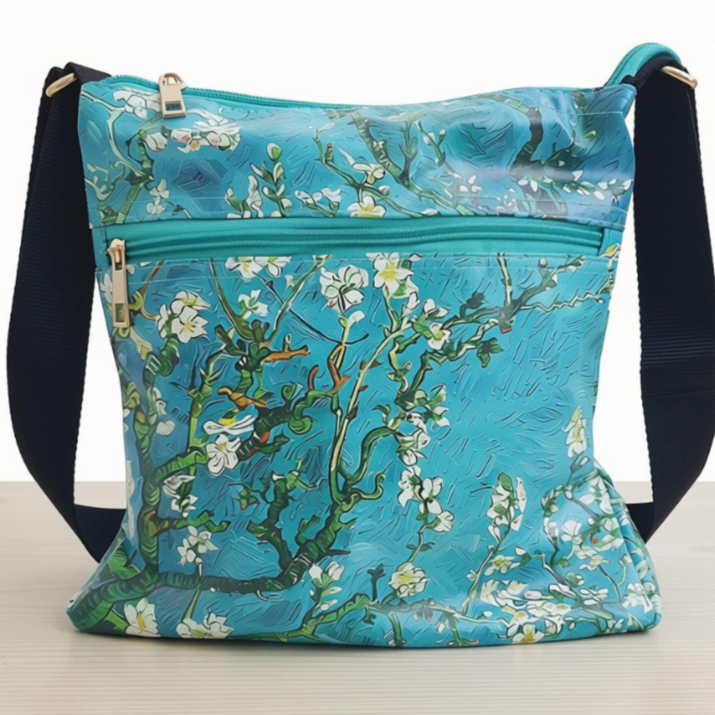 A turquoise blue shoulder bag featuring a Van Gogh-style floral blossom print with white flowers and green branches, complete with a black adjustable shoulder strap and gold-tone hardware.