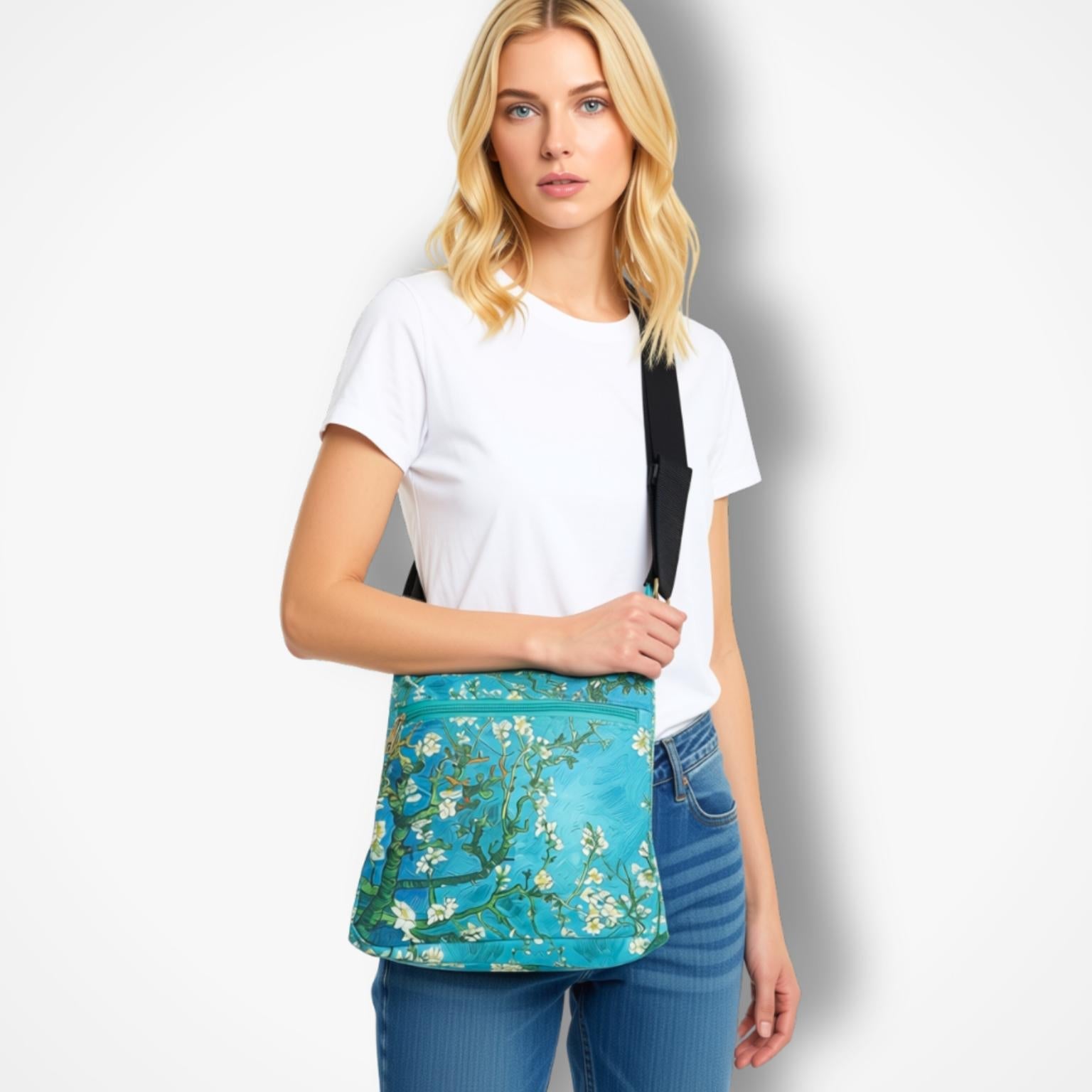 A woman wearing a white t-shirt and blue jeans models a teal crossbody bag with a floral print, set against a plain white studio background.