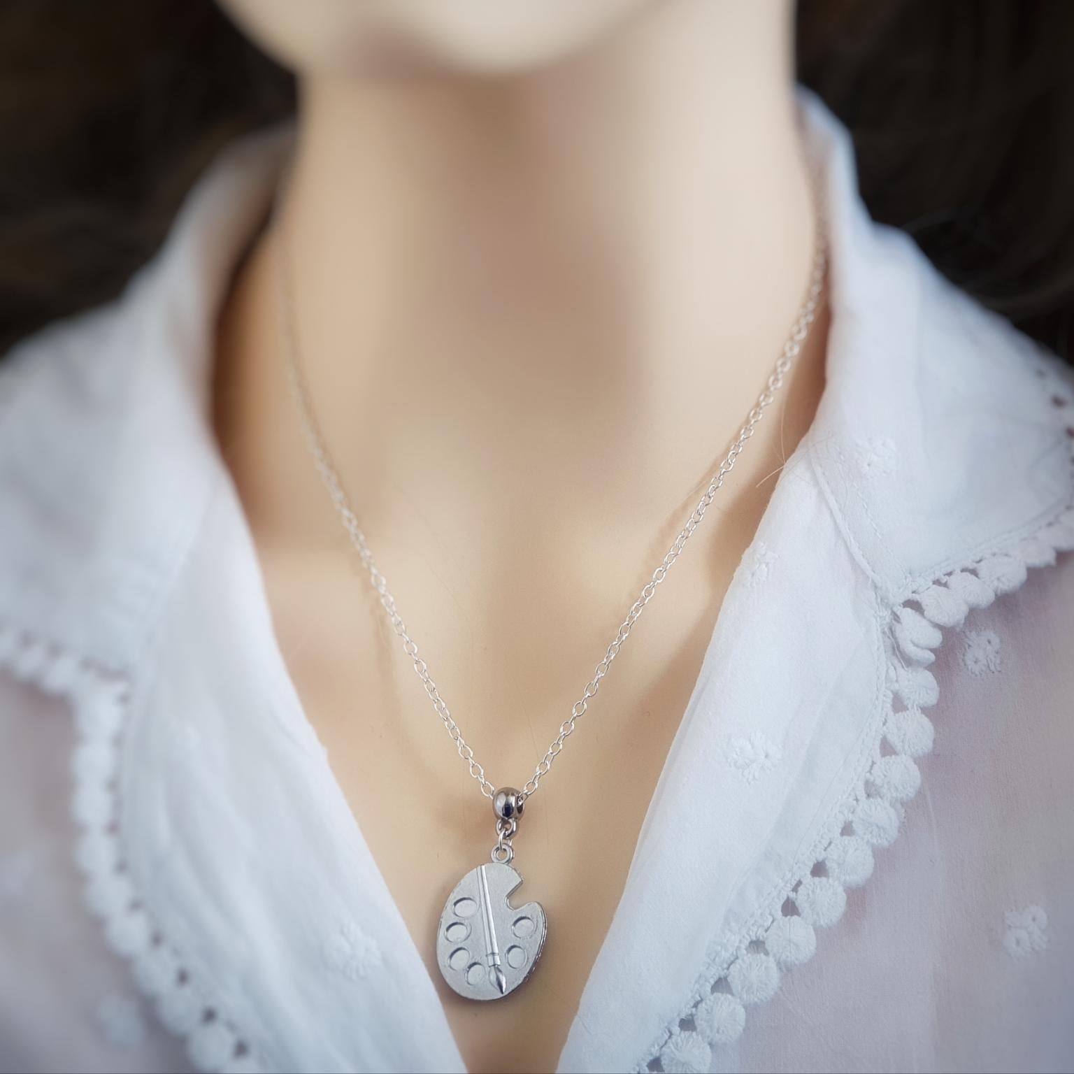 Silver necklace with an artist palette pendant on a mannequin wearing a white blouse.