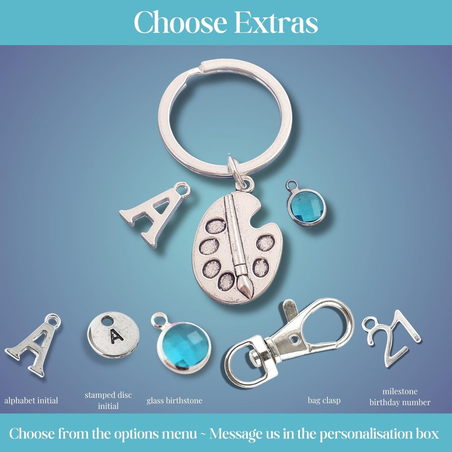 A product options graphic showing a silver keychain with multiple charms, including an artist palette charm, a blue glass birthstone, and customizable letter and number options, under the heading 'Choose Extras'.