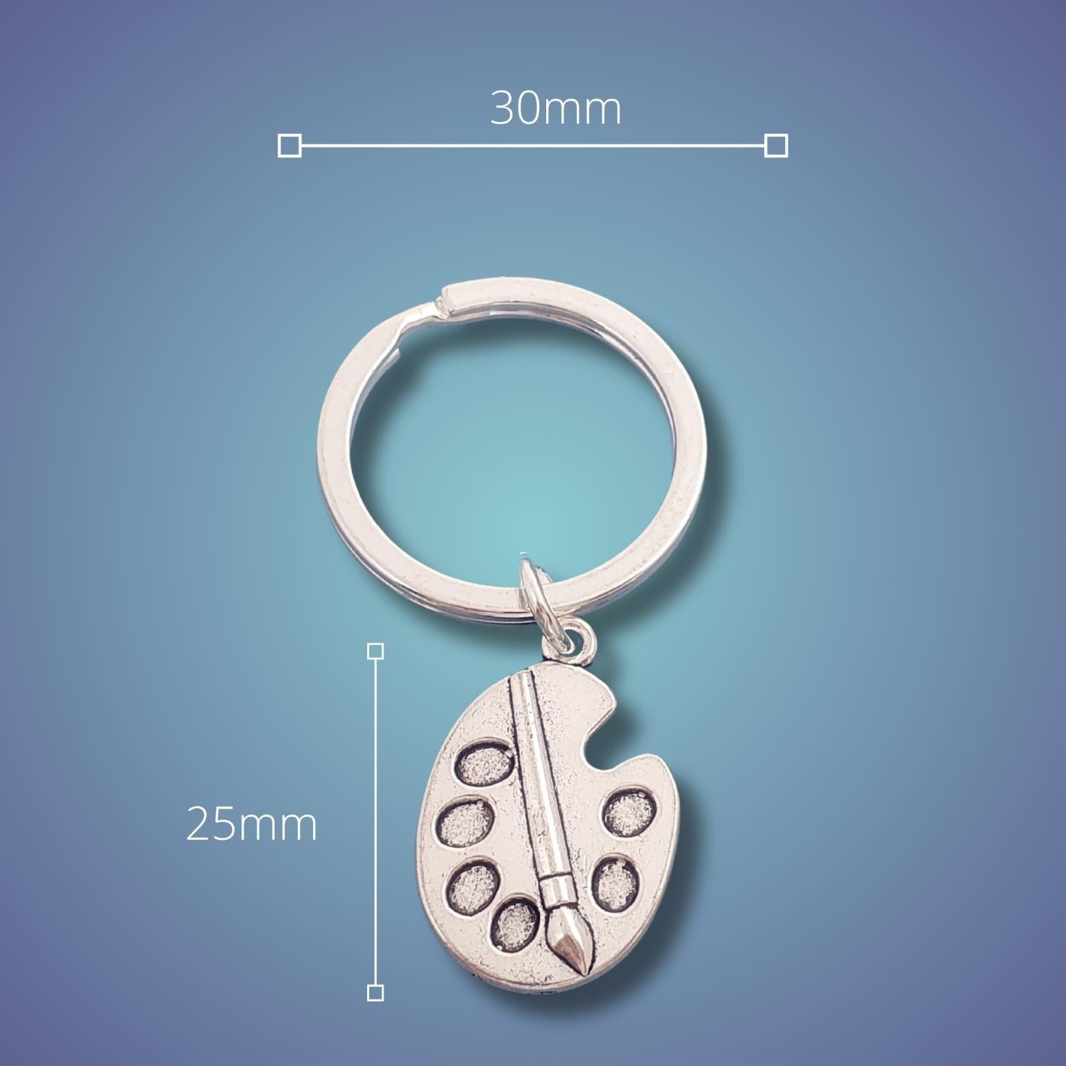 A silver keychain with a small artist paint palette charm and paintbrush detail, shown on a blue gradient background with dimension lines indicating 30mm width and 25mm height.