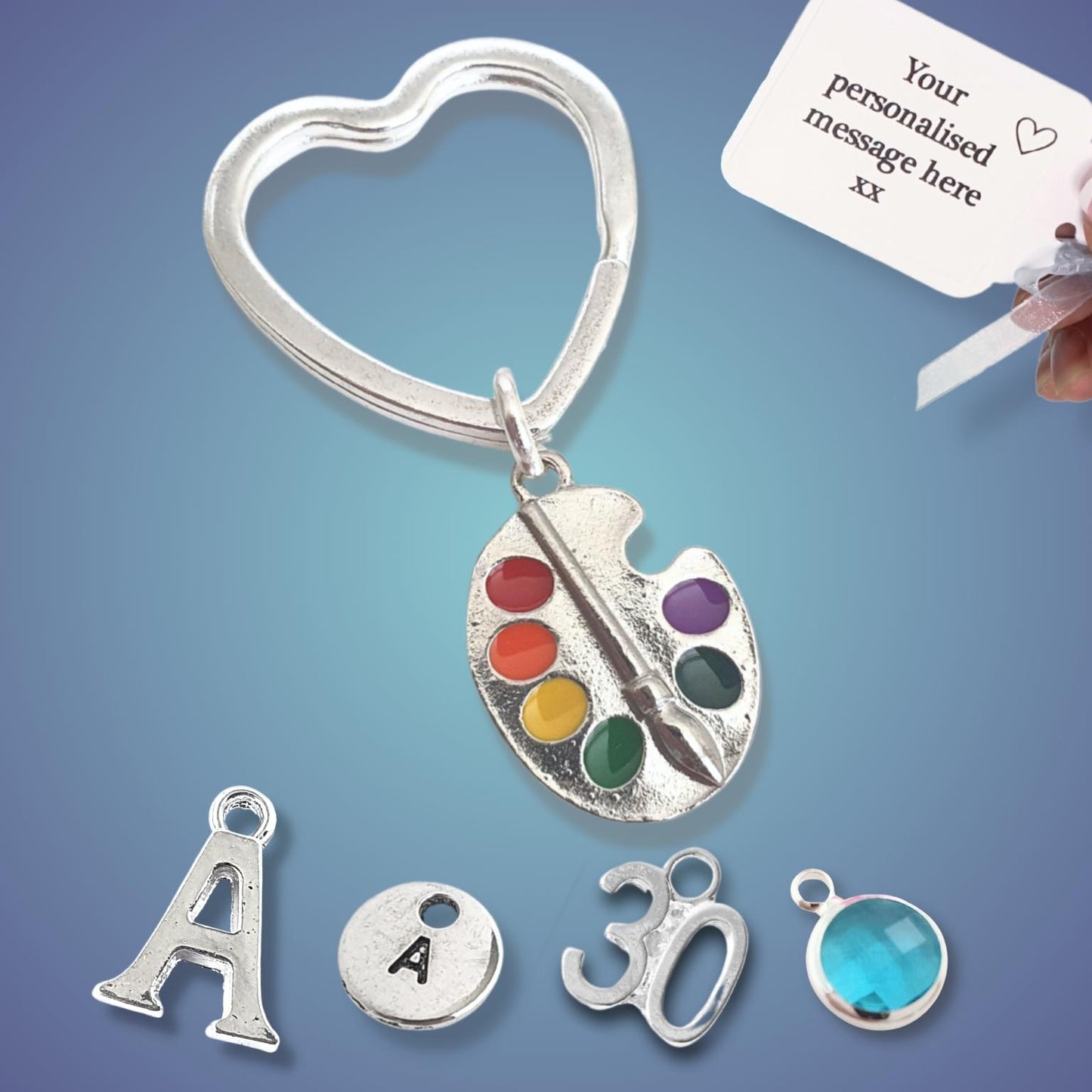 Silver keychain with paint palette, brush, and letter charms on a blue background
