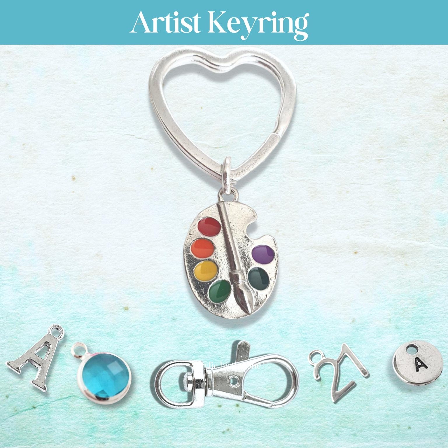 Artist keyring with heart-shaped keychain, paint palette charm, and additional charms on a light blue background.