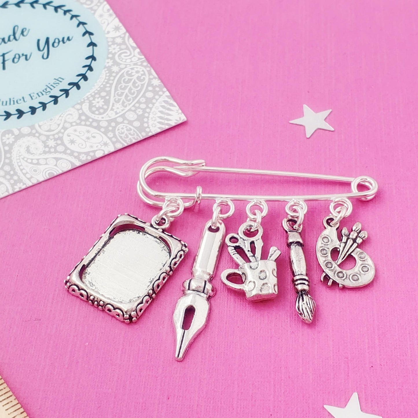 Silver brooch with charms on a pink background