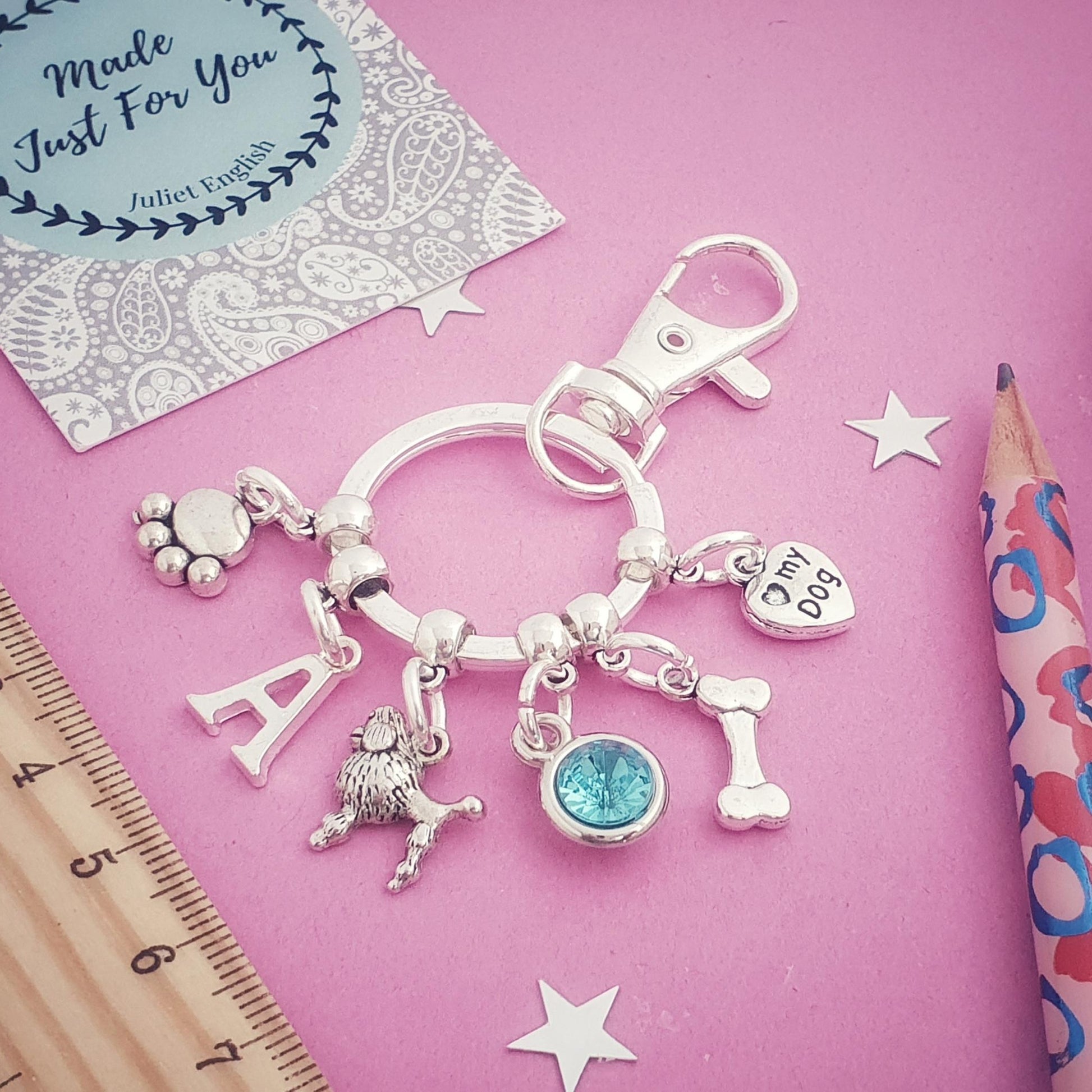 Silver keychain with charms on a pink background with a ruler and pencil.