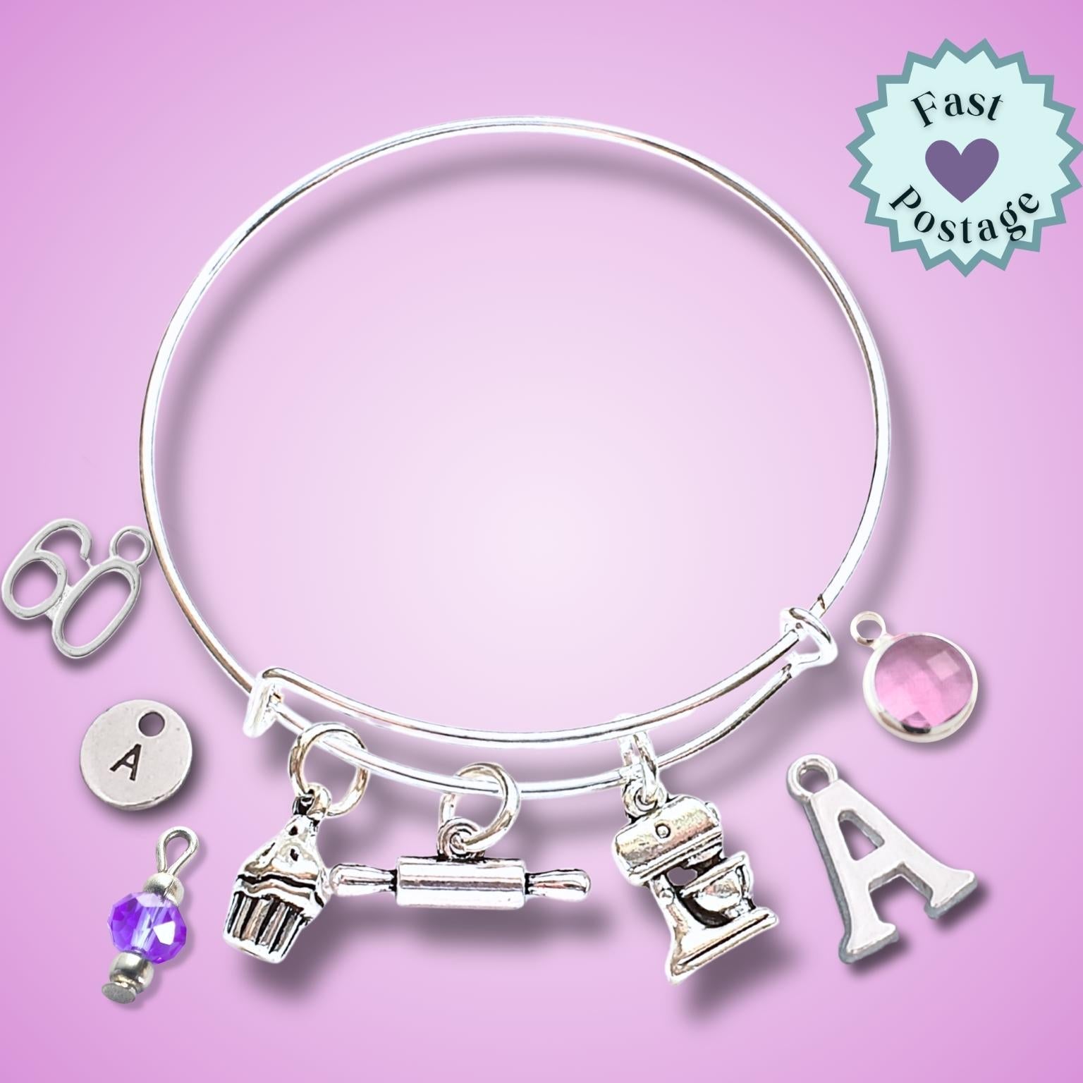 A silver-toned expandable bangle bracelet with multiple charms, including letters, a cupcake, a rolling pin, a mixer, and a pink gem, displayed on a pink background with a 'Fast Postage' badge.