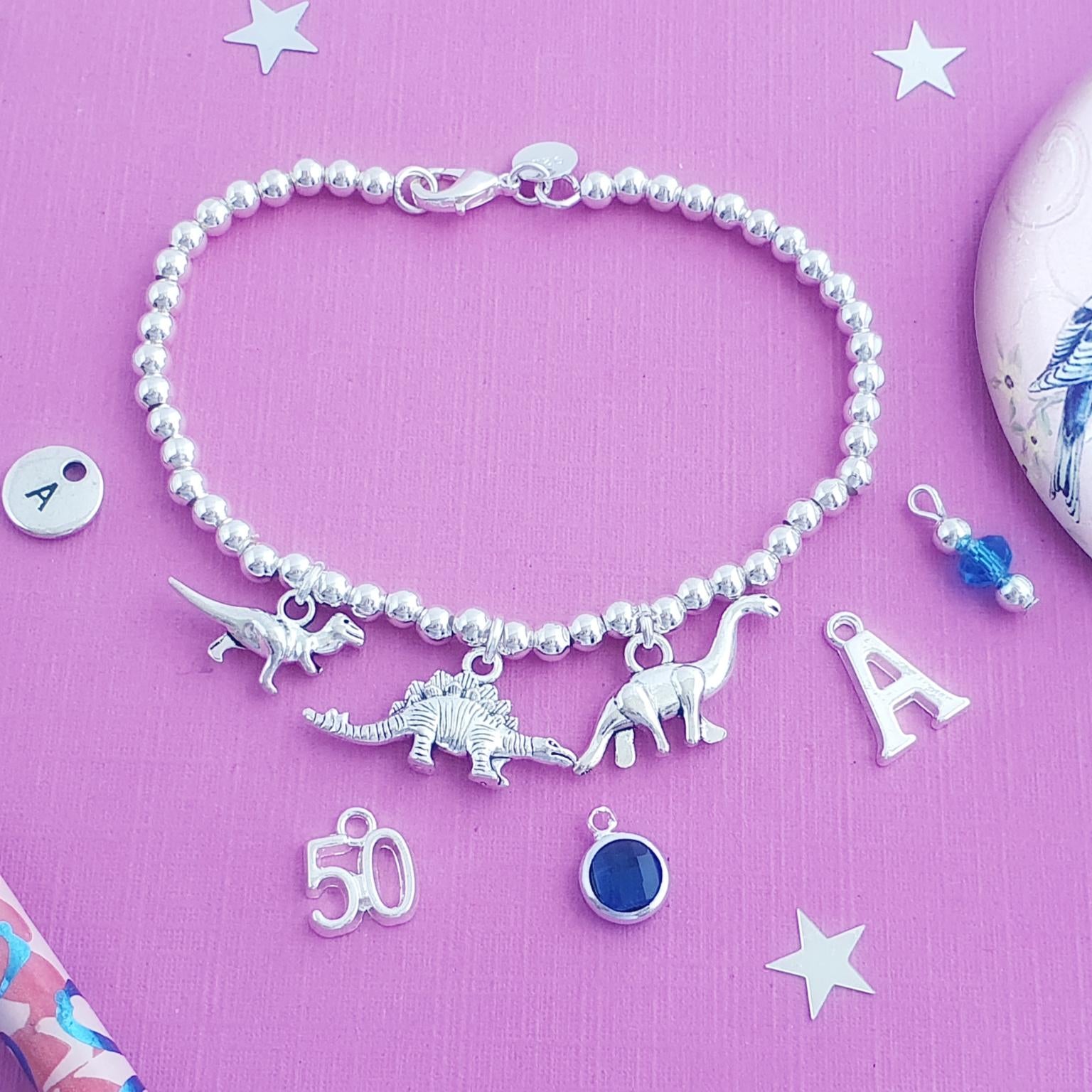 Silver bracelet with dinosaur charms on a pink background
