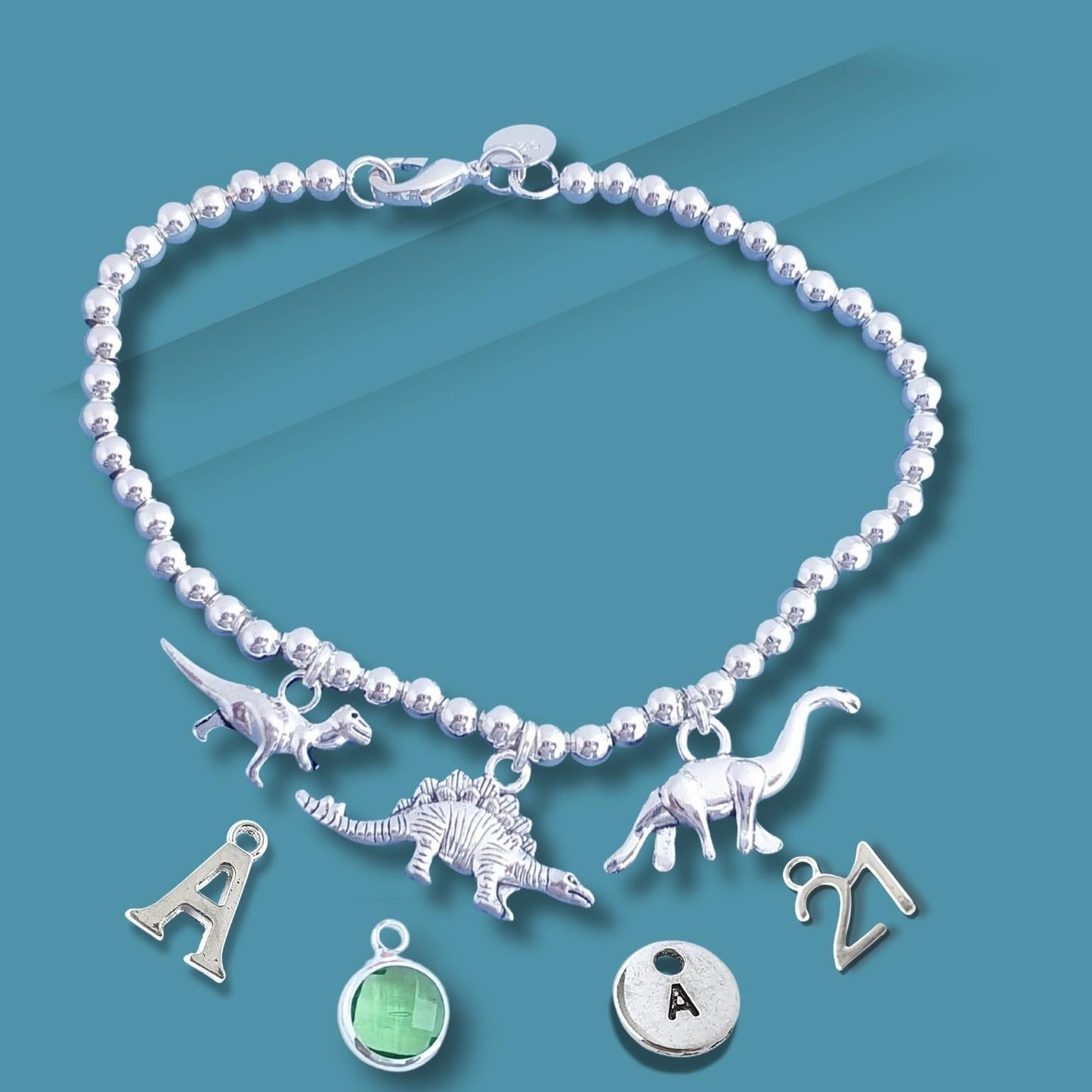 Silver beaded bracelet with dinosaur and letter charms on a blue background