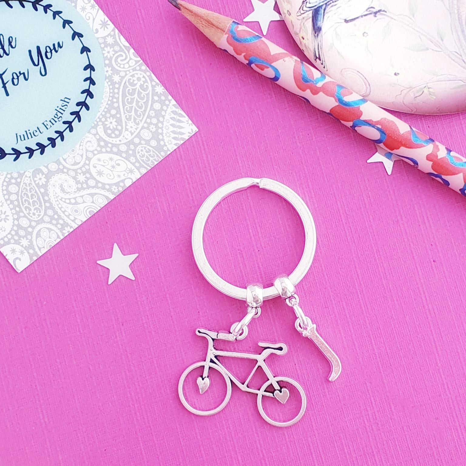 Keychain with bicycle charm on a pink surface with a card and pencils.