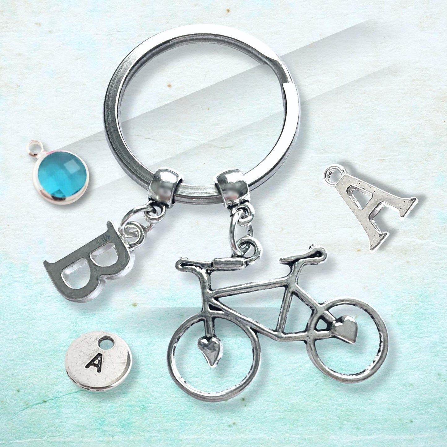 Silver keychain with bicycle, letter 'B', and letter 'A' charms on a light blue background