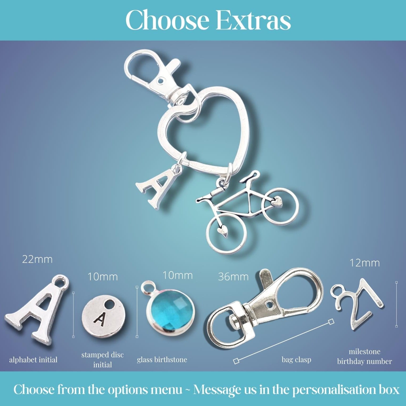 Silver keychain customization options under the heading 'Choose Extras' on a blue gradient background. The image shows a heart-shaped key ring with an 'A' and bicycle charm, plus smaller size and shape options for alphabet initial, stamped disc initial, glass birthstone, bag clip, and milestone birthday number with measurements in millimeters.