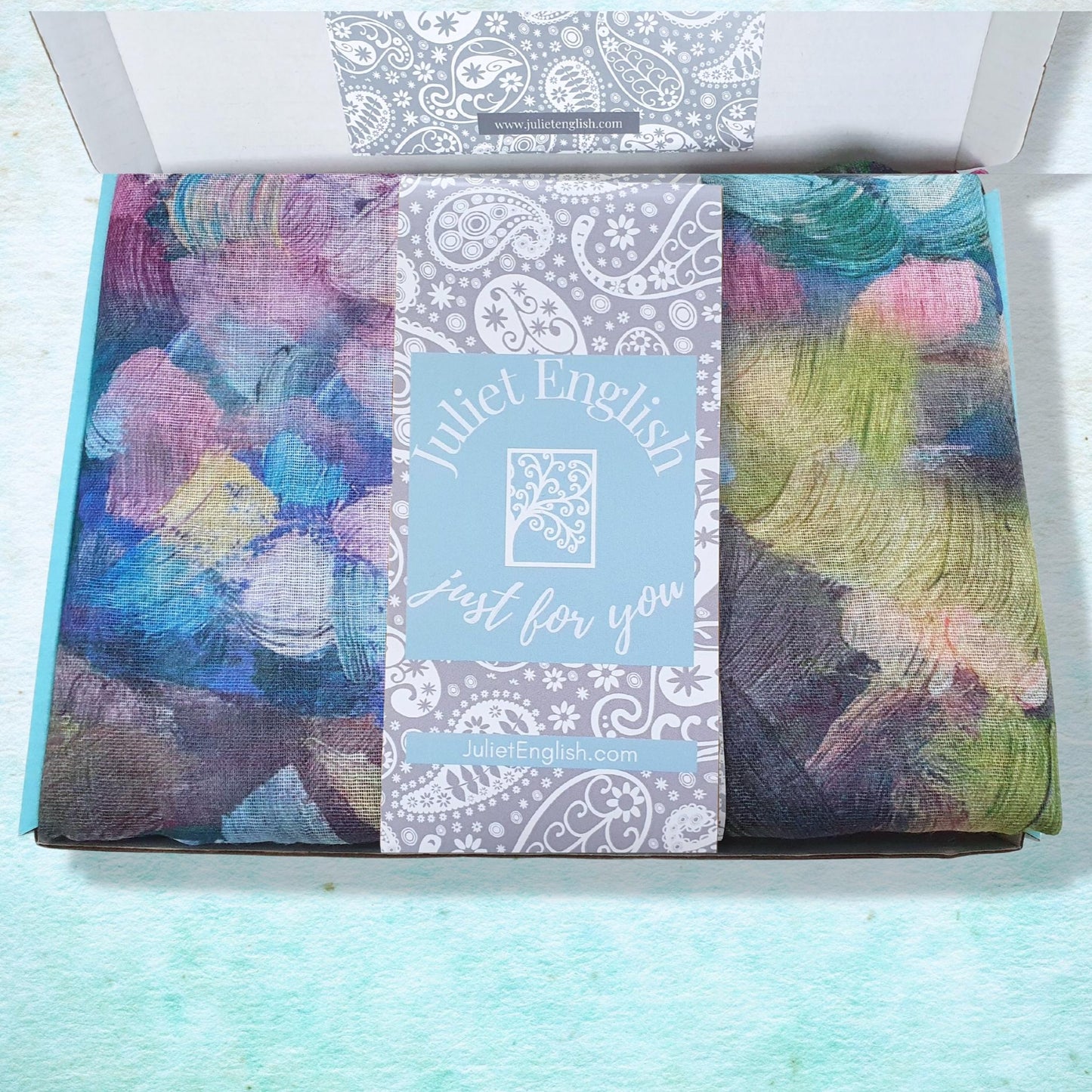 Folded scarf with colorful pattern in a box and a visible brand label on a light blue background