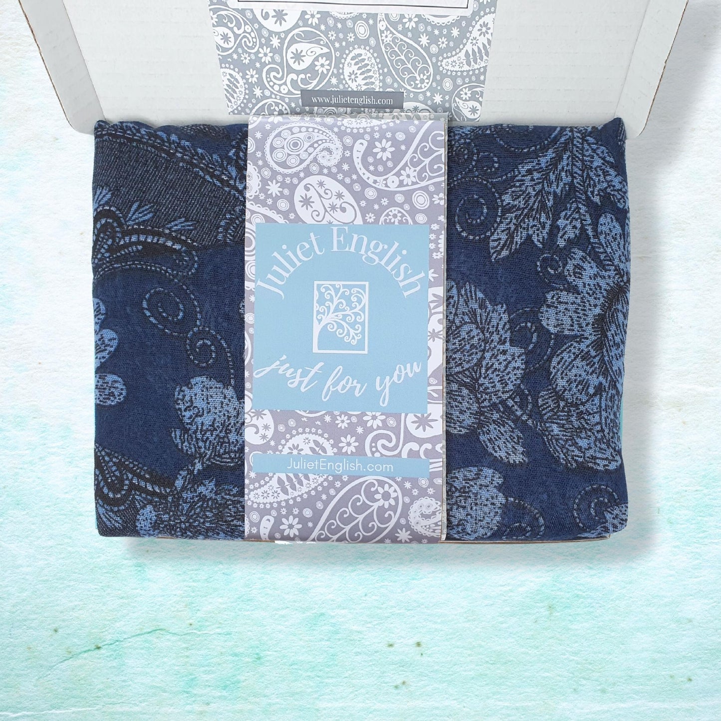 Lightweight scarf with blue and grey paisley patterns in a box on a light blue background
