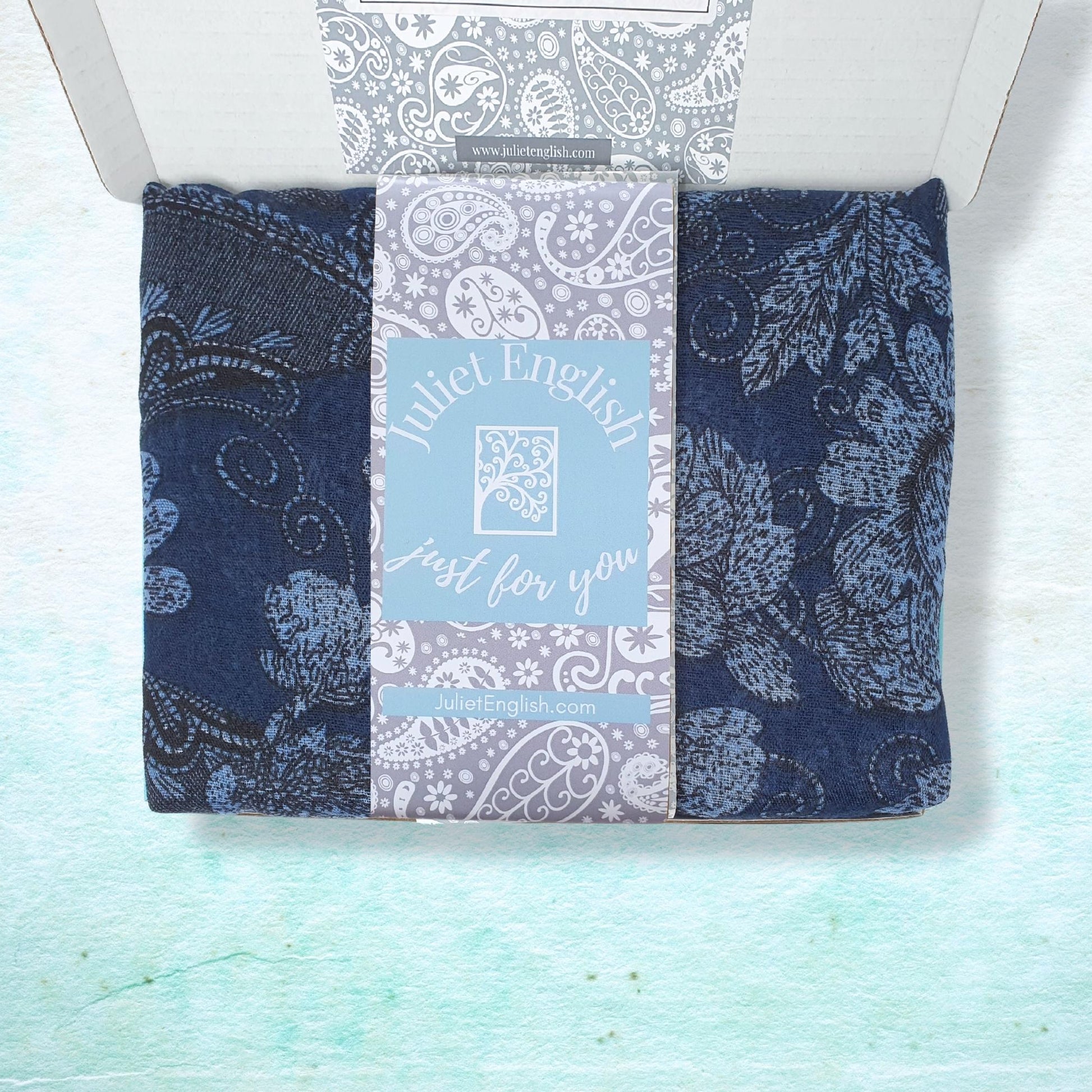 Lightweight scarf with blue and grey paisley patterns in a box on a light blue background