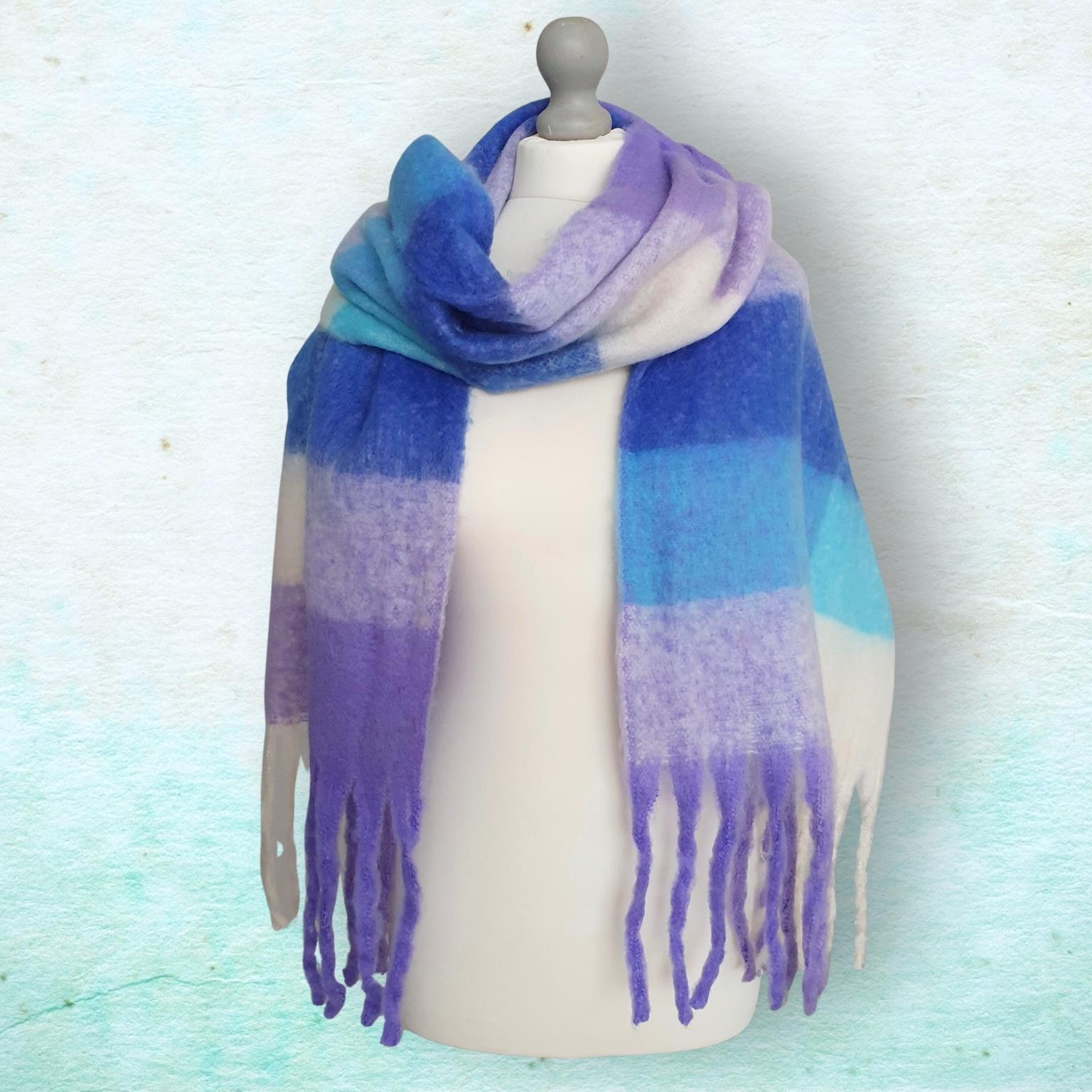 Mannequin wearing a blue and purple checked scarf with fringe on a light blue background