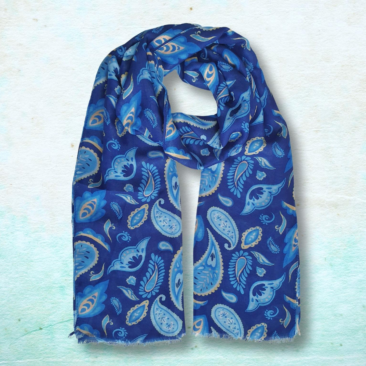 A blue paisley scarf with light blue and beige accents, draped against a textured light blue background.