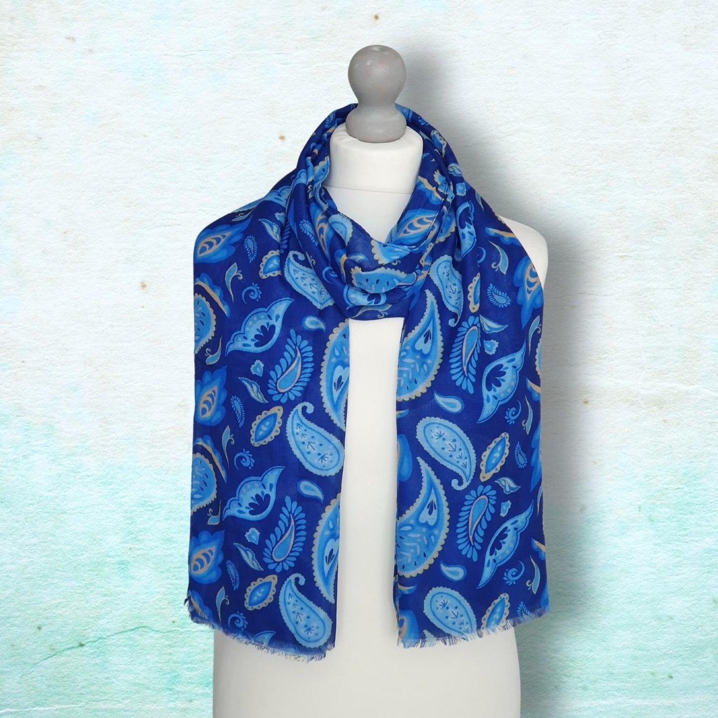A blue and light blue paisley patterned scarf draped on a white mannequin torso against a textured light blue background.