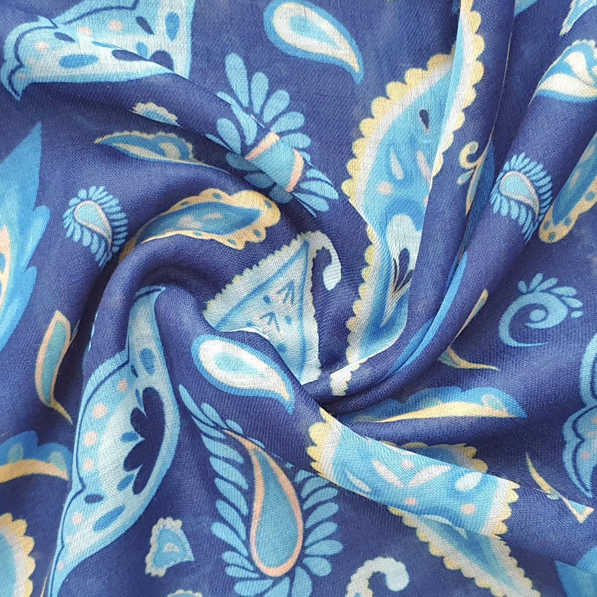 A close-up of draped scarf fabric with a paisley pattern in blue, light blue, and beige on a dark blue background.