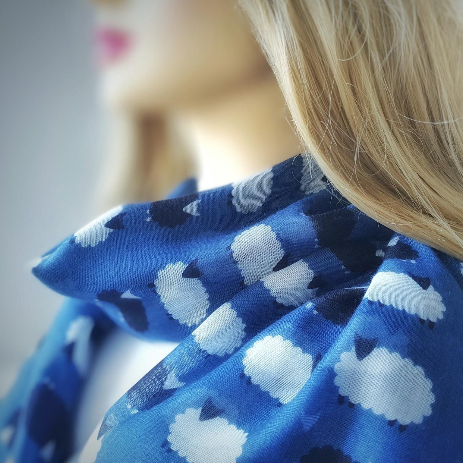 Close-up of a blue scarf with white sheep pattern worn by a person
