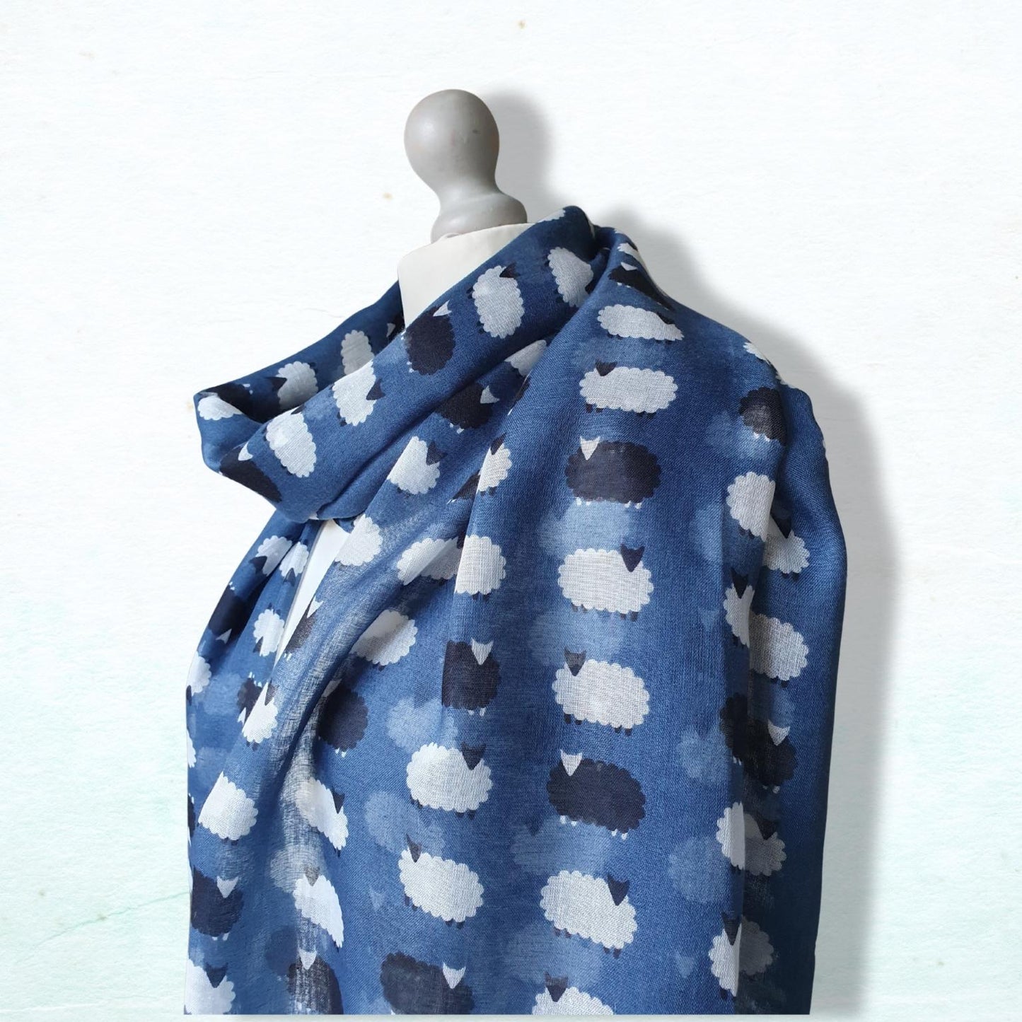 Blue scarf with sheep pattern draped over a mannequin on a white background