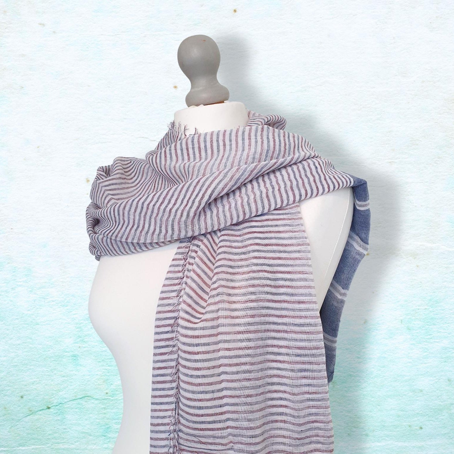 Mannequin wearing a striped scarf against a light blue textured background