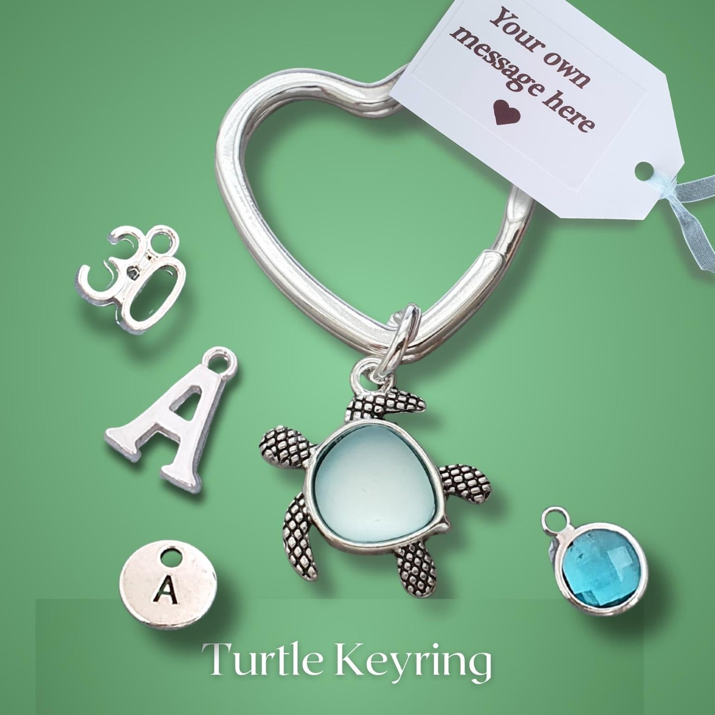Silver turtle keyring with a heart-shaped clasp, a sea turtle charm, and customizable initial letter charms on a green background.