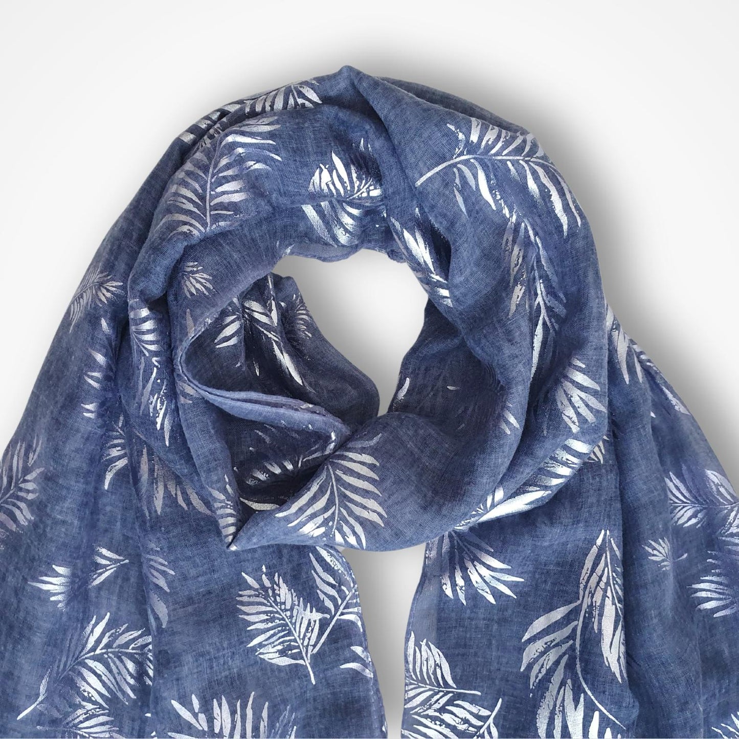A lightweight blue scarf with a silver palm leaf pattern, draped in a loose loop against a clean white background.