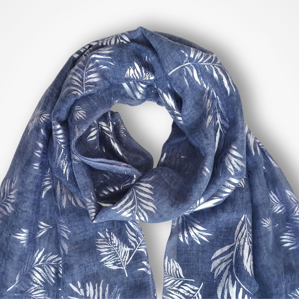 A lightweight blue scarf with a silver palm leaf pattern, draped in a loose loop against a clean white background.