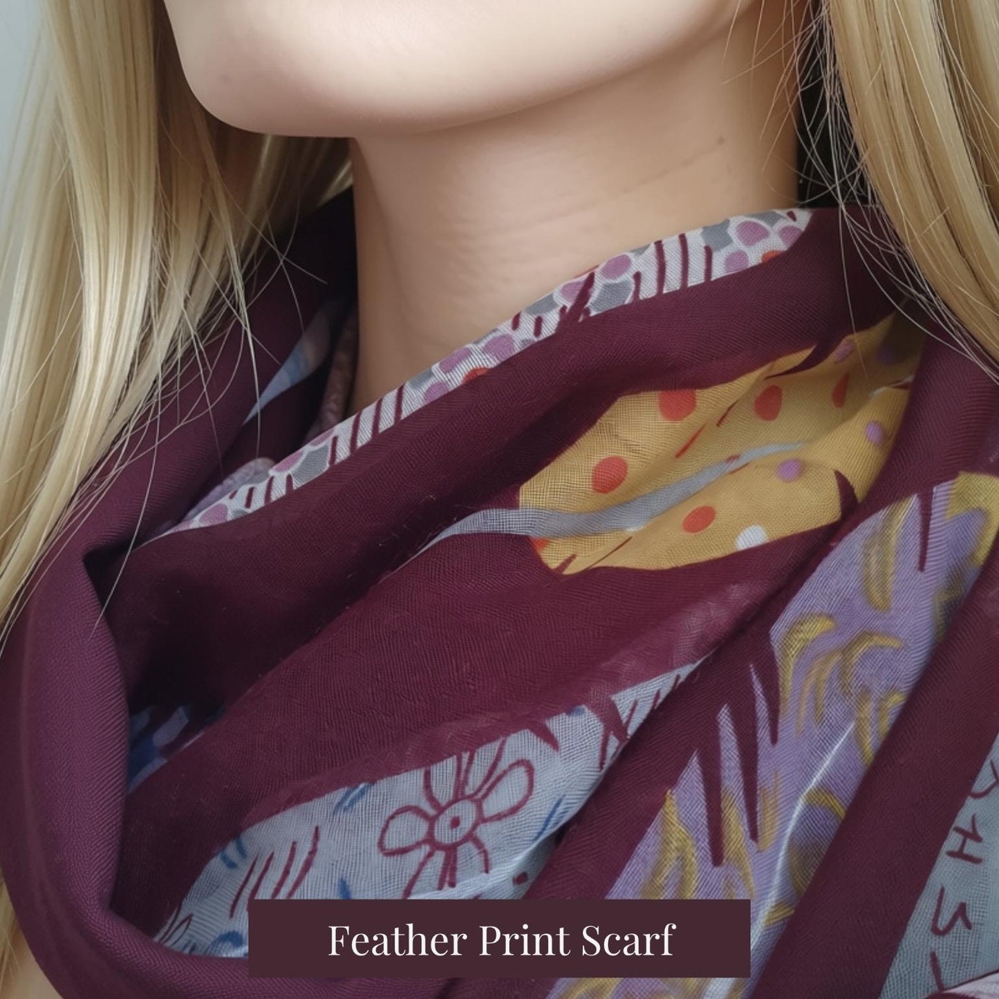 A close-up of a woman wearing a feather print scarf in deep burgundy, lavender, yellow, and gray. The image features a text overlay at the bottom that reads 'Feather Print Scarf'.
