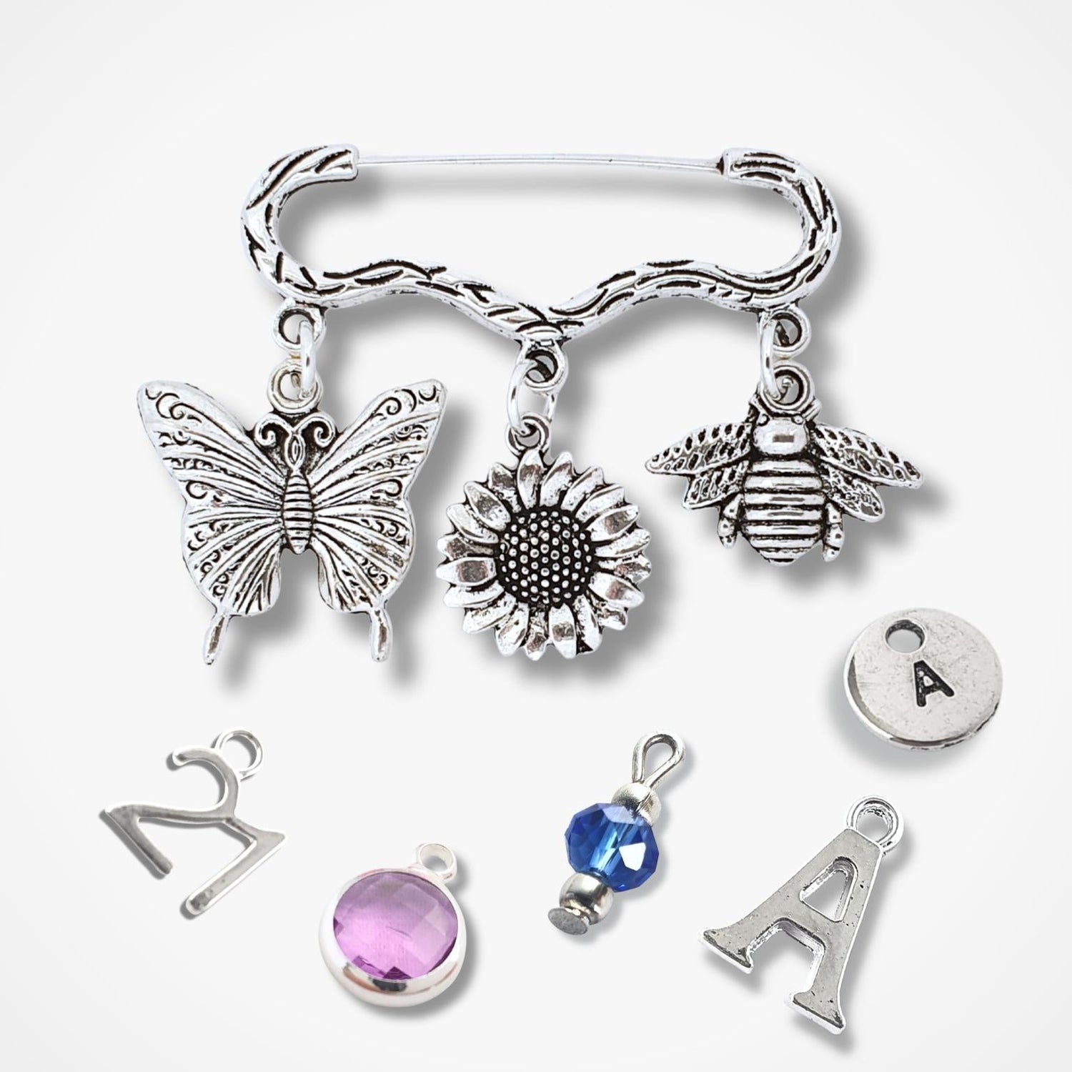 Brooch with silver charms including a butterfly, sunflower, bee, and letter 'A' on a white background.