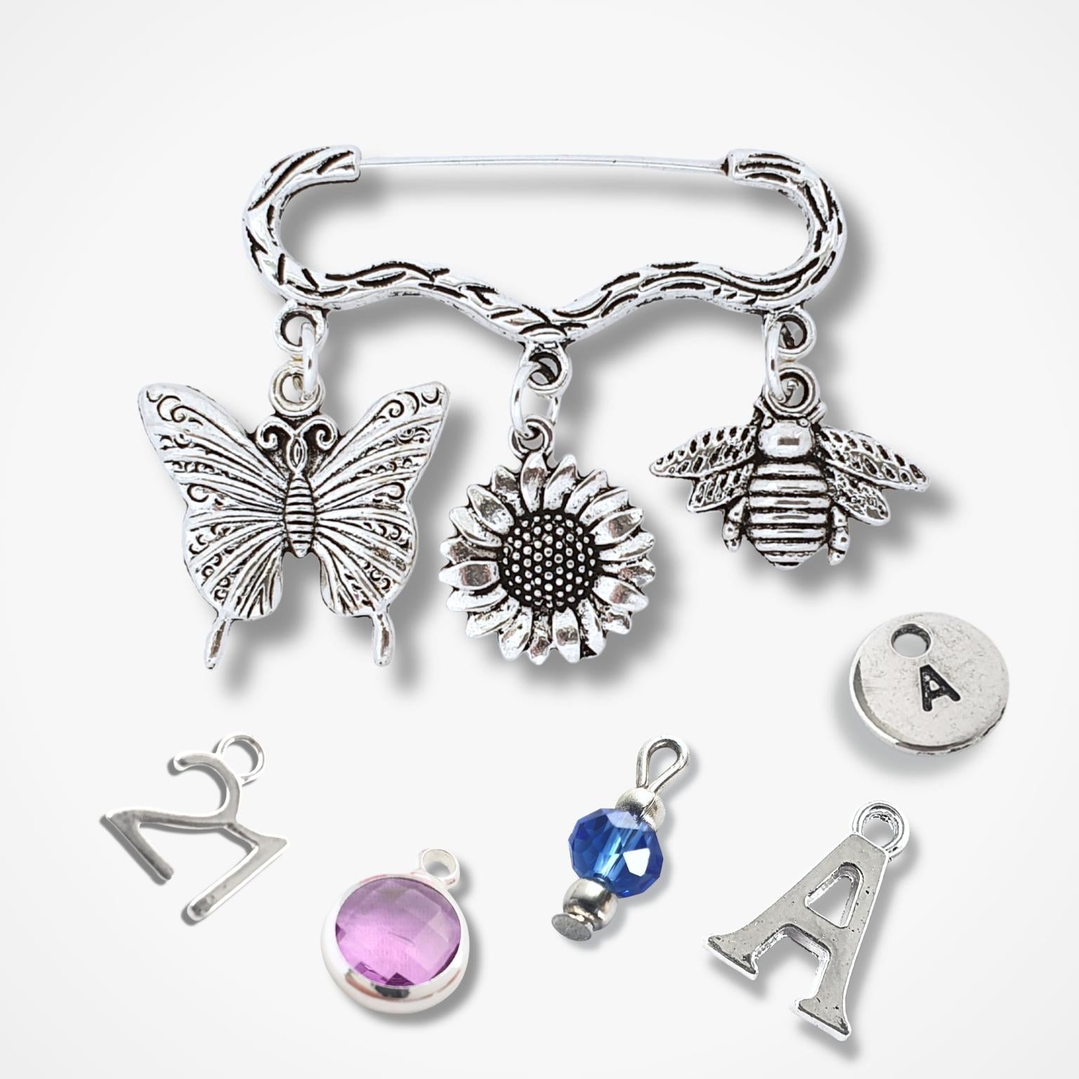 Brooch with silver charms including a butterfly, sunflower, bee, and letter 'A' on a white background.