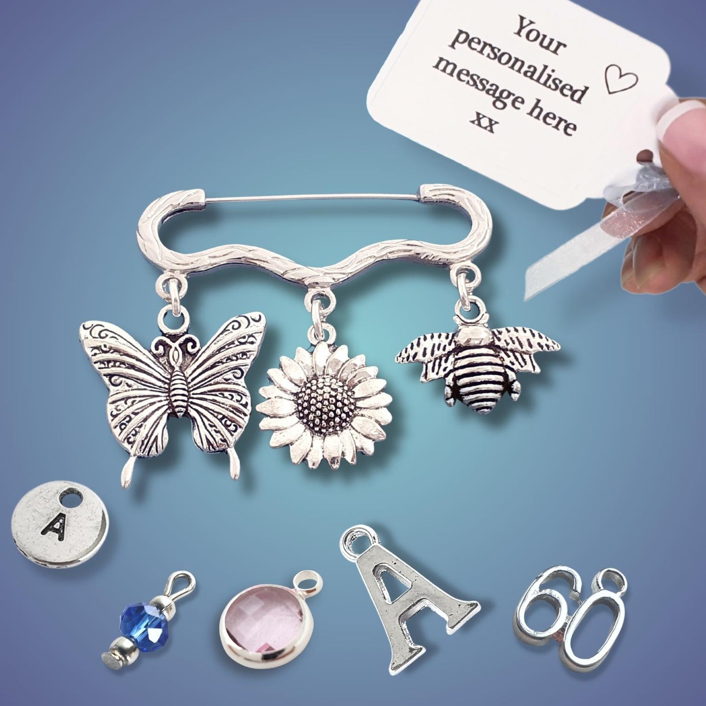 Silver charm brooch with butterfly, sunflower, and bee charms on a blue background.