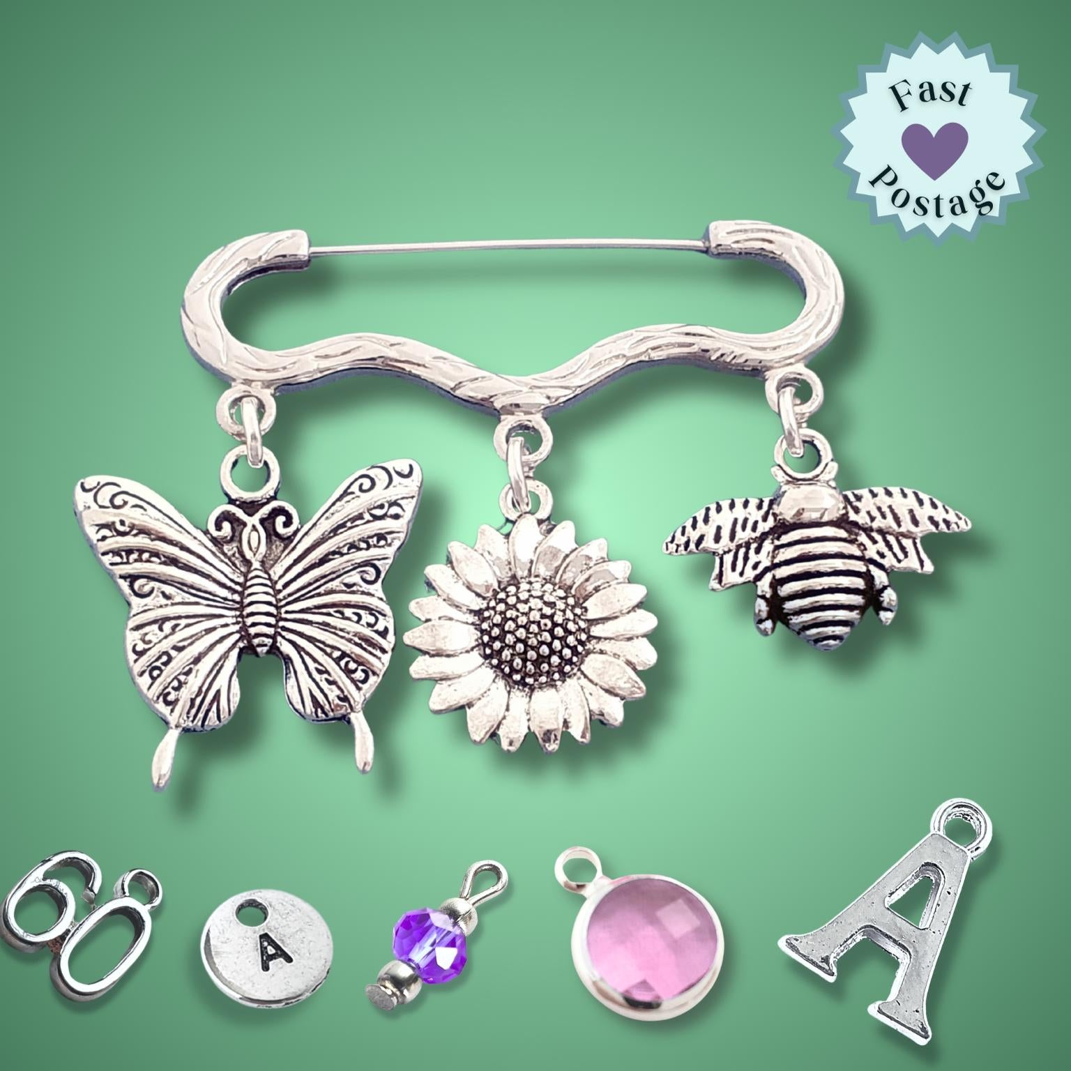 Silver brooch with butterfly, sunflower, and bee charms on a green background