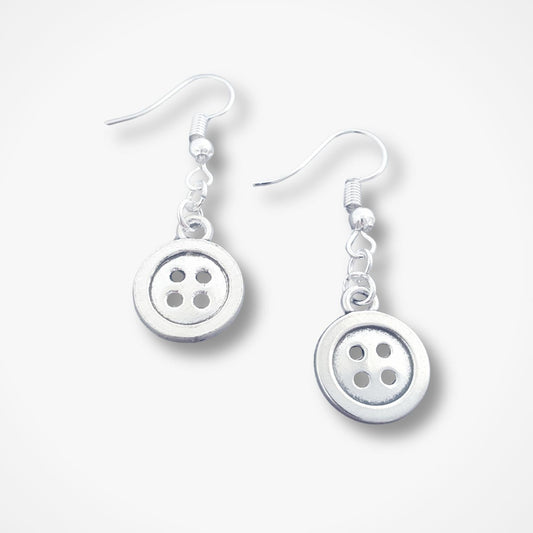 A pair of silver dangle earrings featuring round button-shaped charms with four holes, suspended from silver fishhook wires, shown on a light gray background.