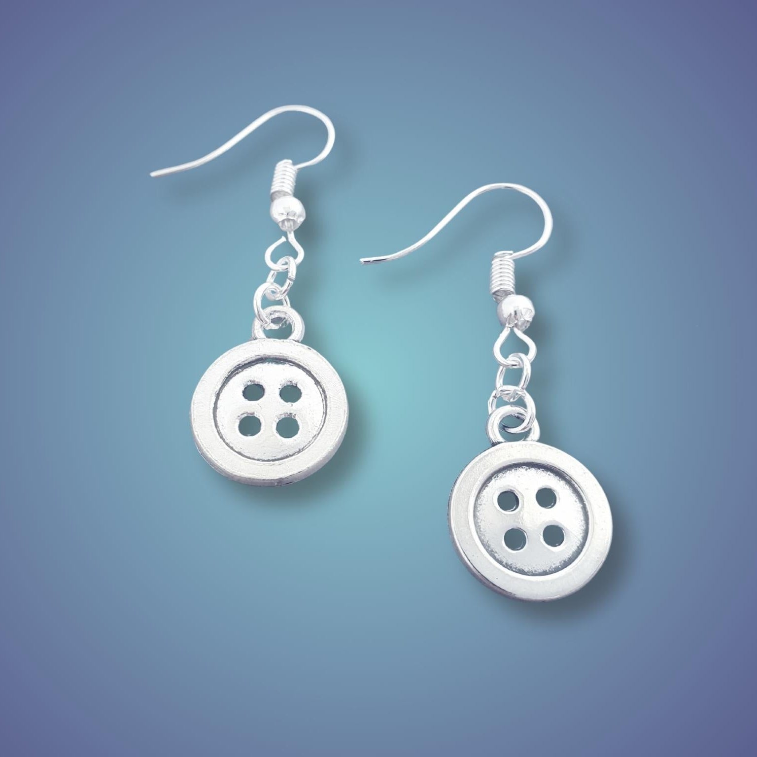 A pair of silver button dangle earrings with four holes, suspended from silver fishhook wires, shown against a blue gradient background.