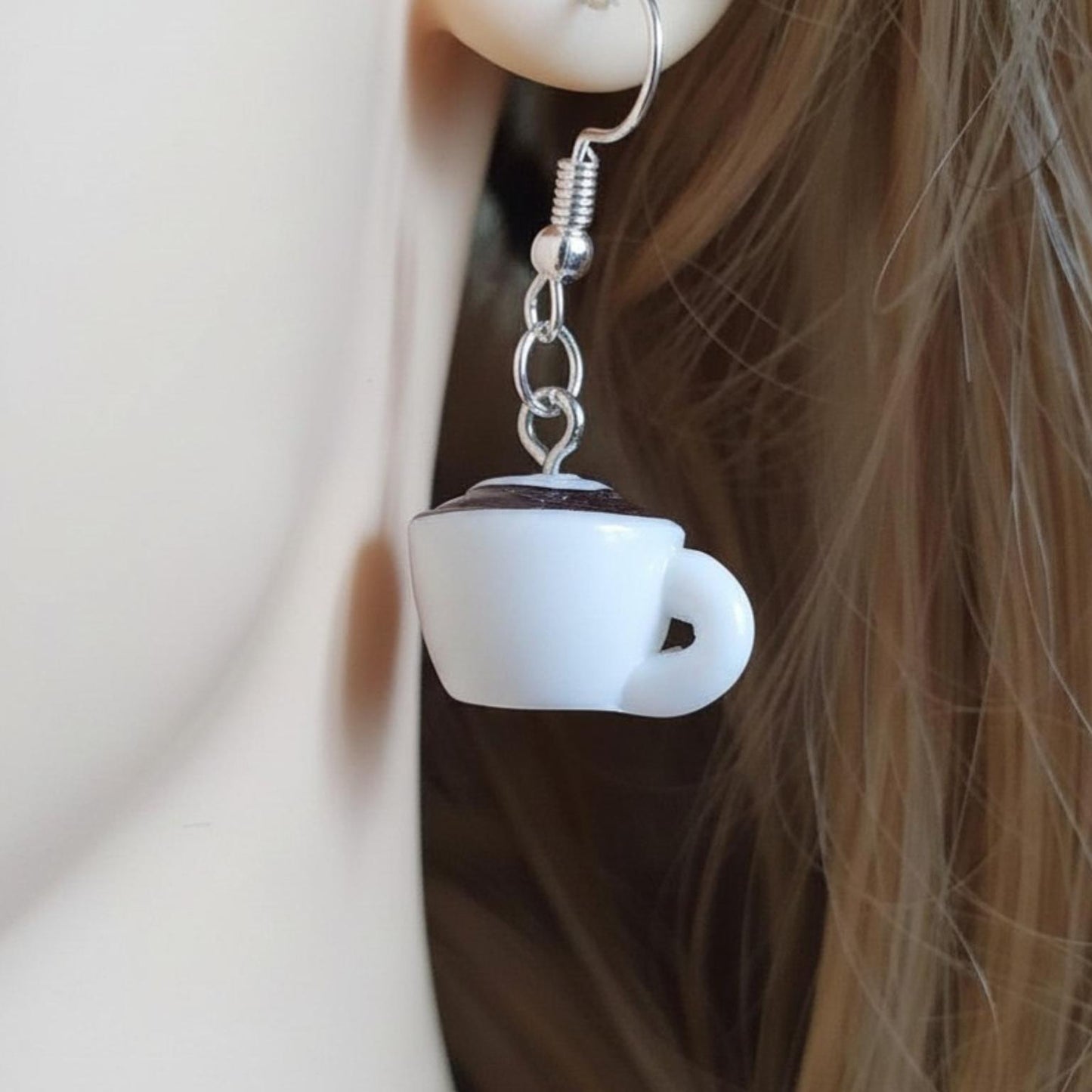 White coffee cup-shaped earring on a blurred background