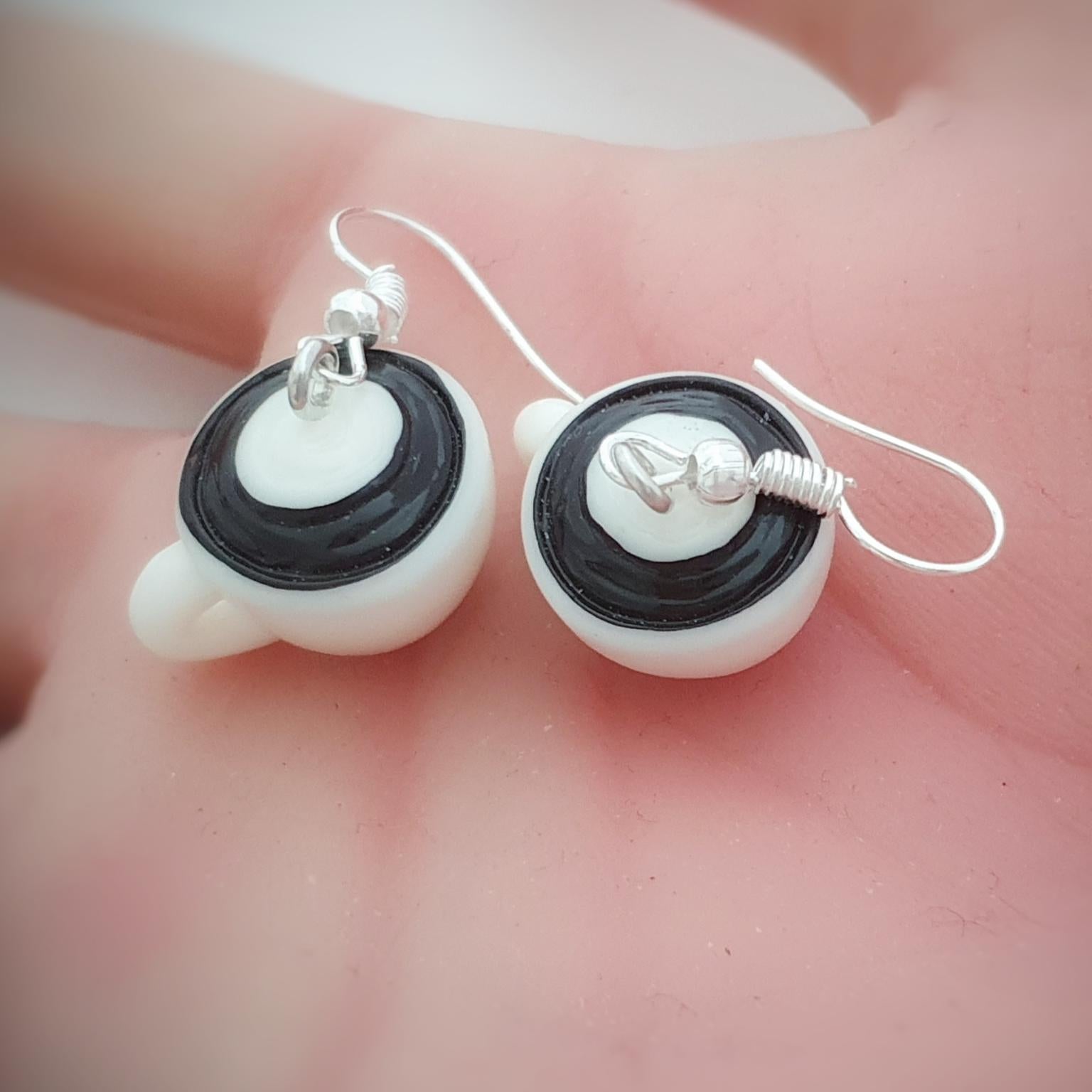 Pair of coffee cup earrings on a hand background