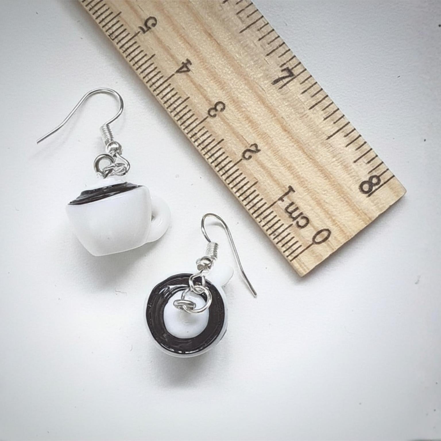 Pair of coffee cup earrings with a wooden ruler for scale on a light grey background