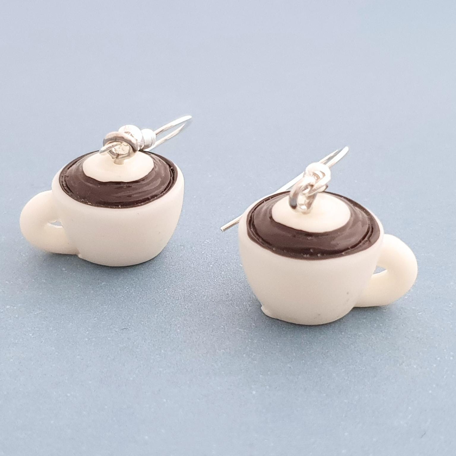 Coffee cup shaped earrings on a light blue background
