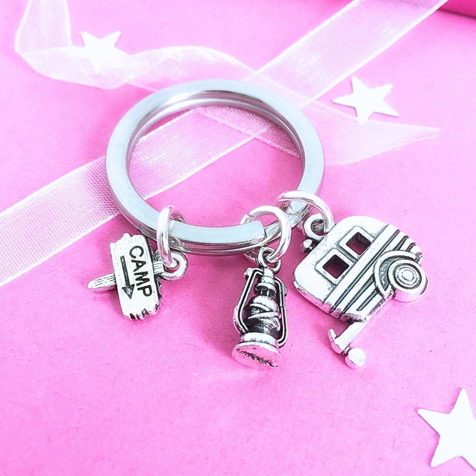 Silver keychain with caravan and camping charms on a pink background