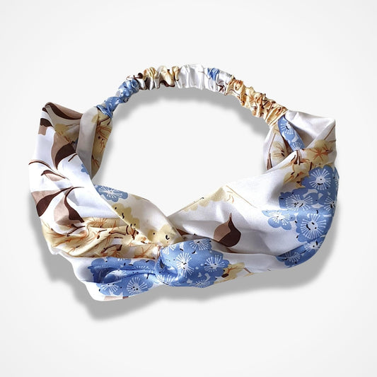 A knotted fabric headband with a white base and a pattern of blue floral motifs and brown abstract shapes, displayed on a light gray background.
