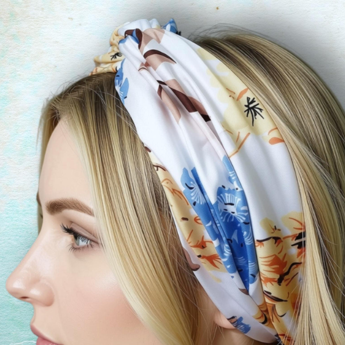 A close-up side profile of a woman with blonde hair wearing a gathered, twisted headband with a blue, beige, and brown floral pattern against a light textured background.