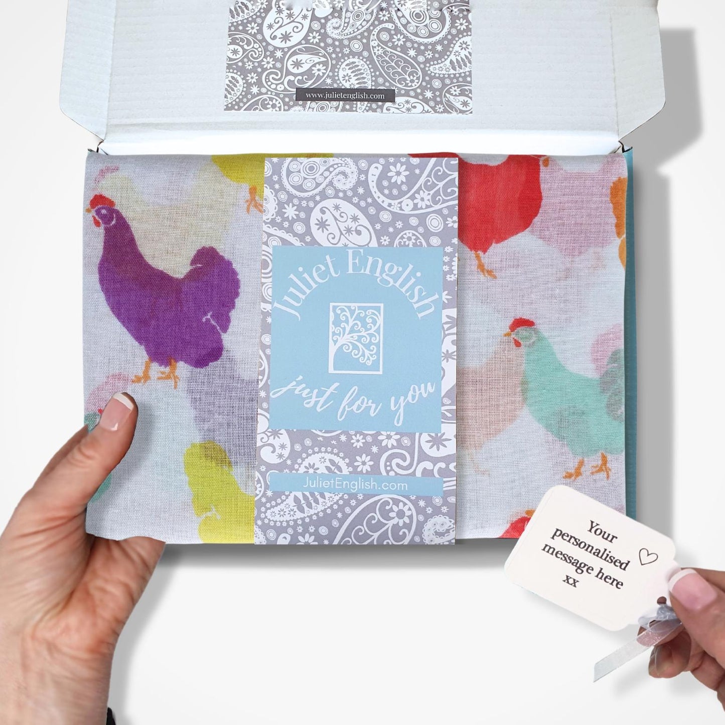 Hand holding a colourful patterned scarf in a box with a card on a white background