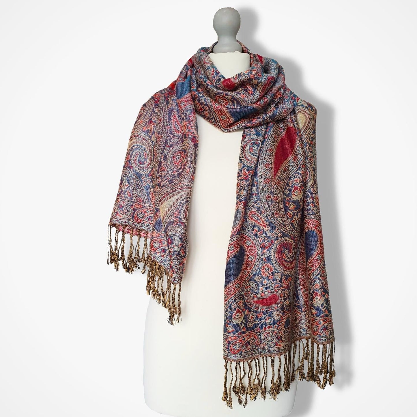 A multicolor paisley scarf with brown fringe, draped on a white mannequin torso against a light gray background.