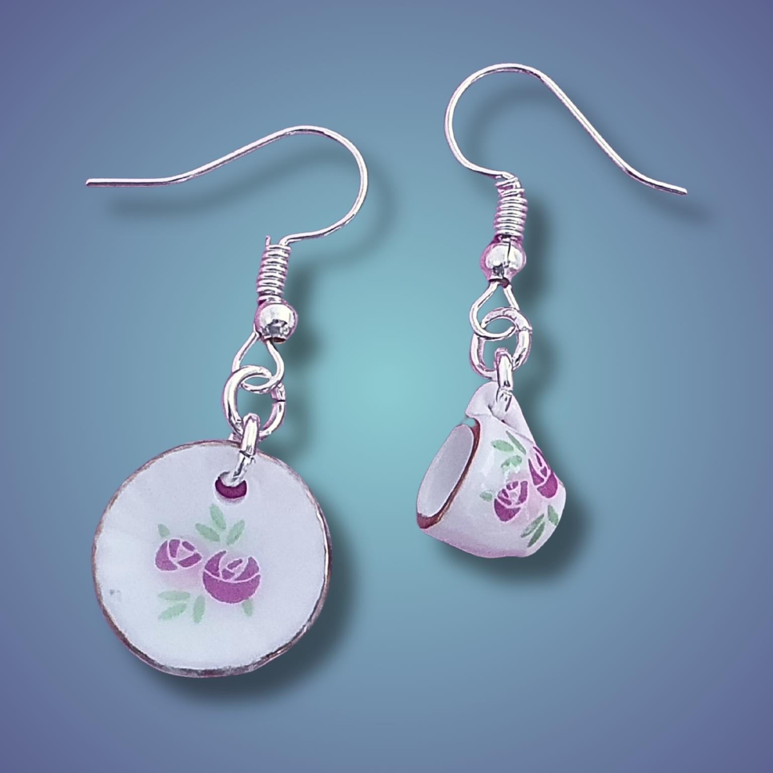 Pair of cup and saucer earrings with floral designs on a gradient blue background