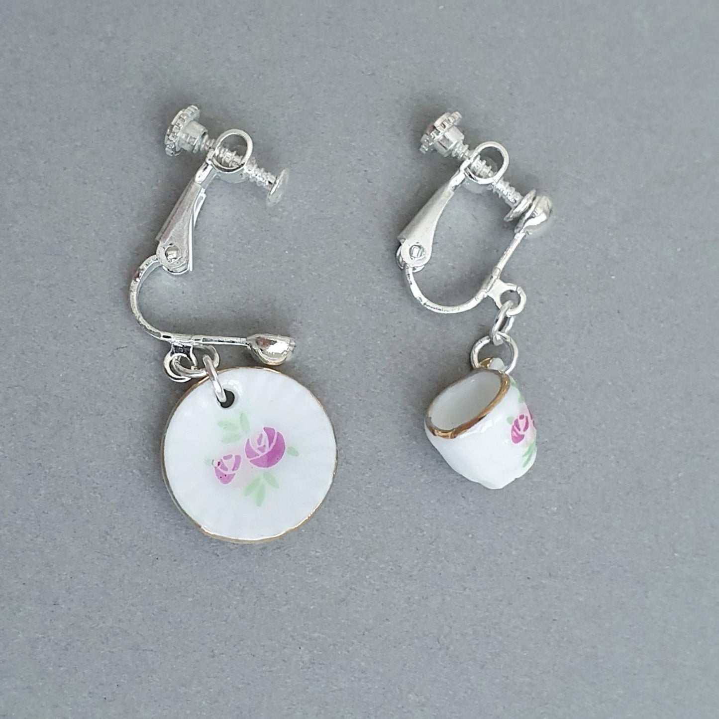 Pair of cup and saucer earrings with floral designs on a grey background