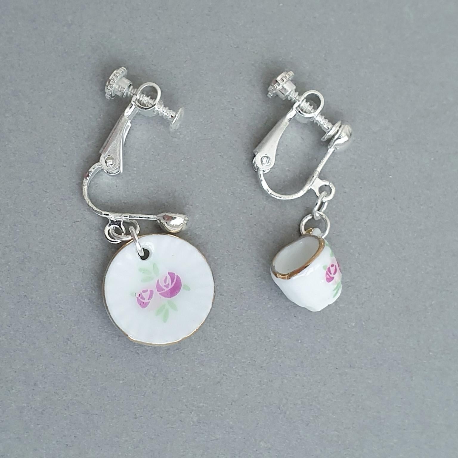 Pair of cup and saucer earrings with floral designs on a grey background