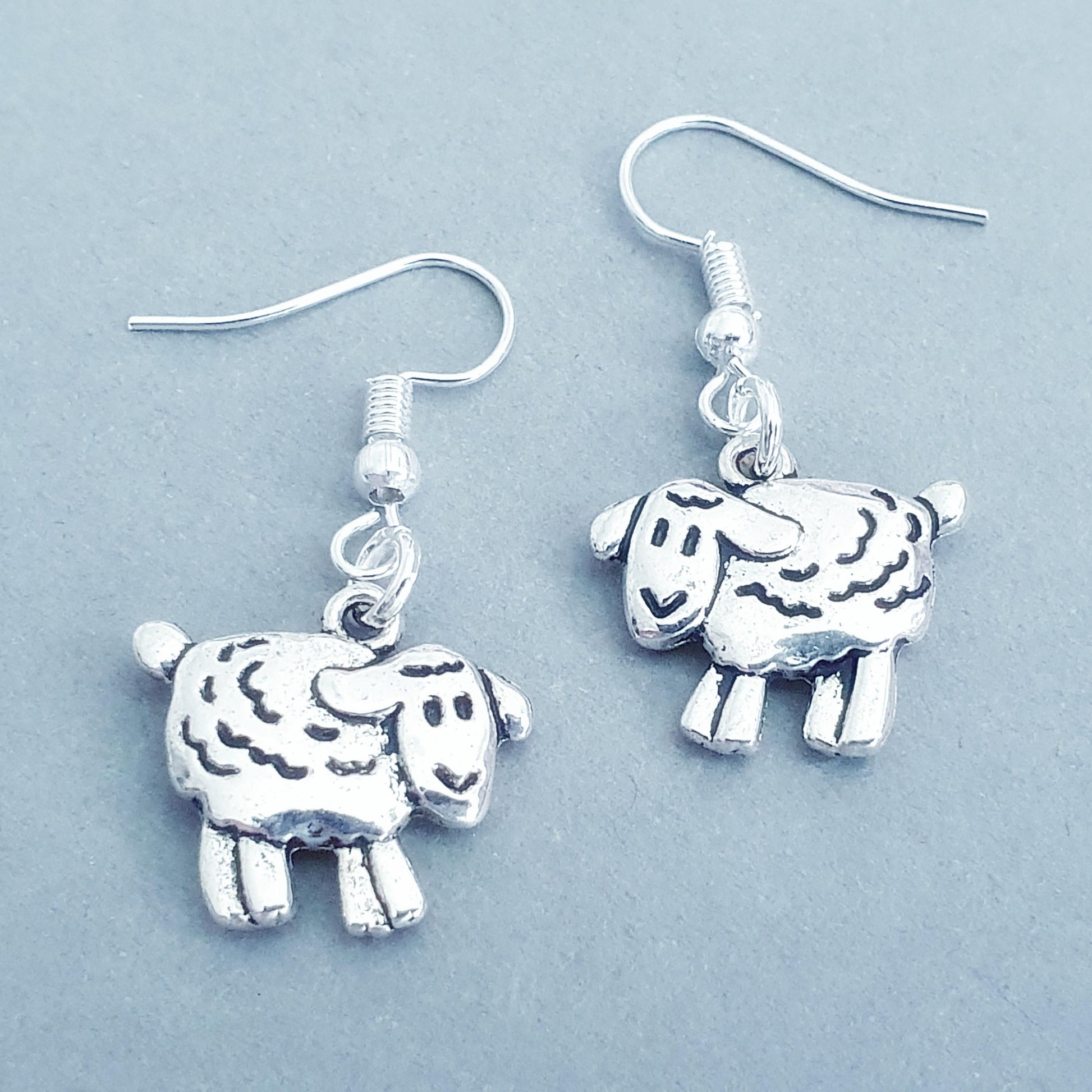 Silver sheep-shaped earrings on a light blue background