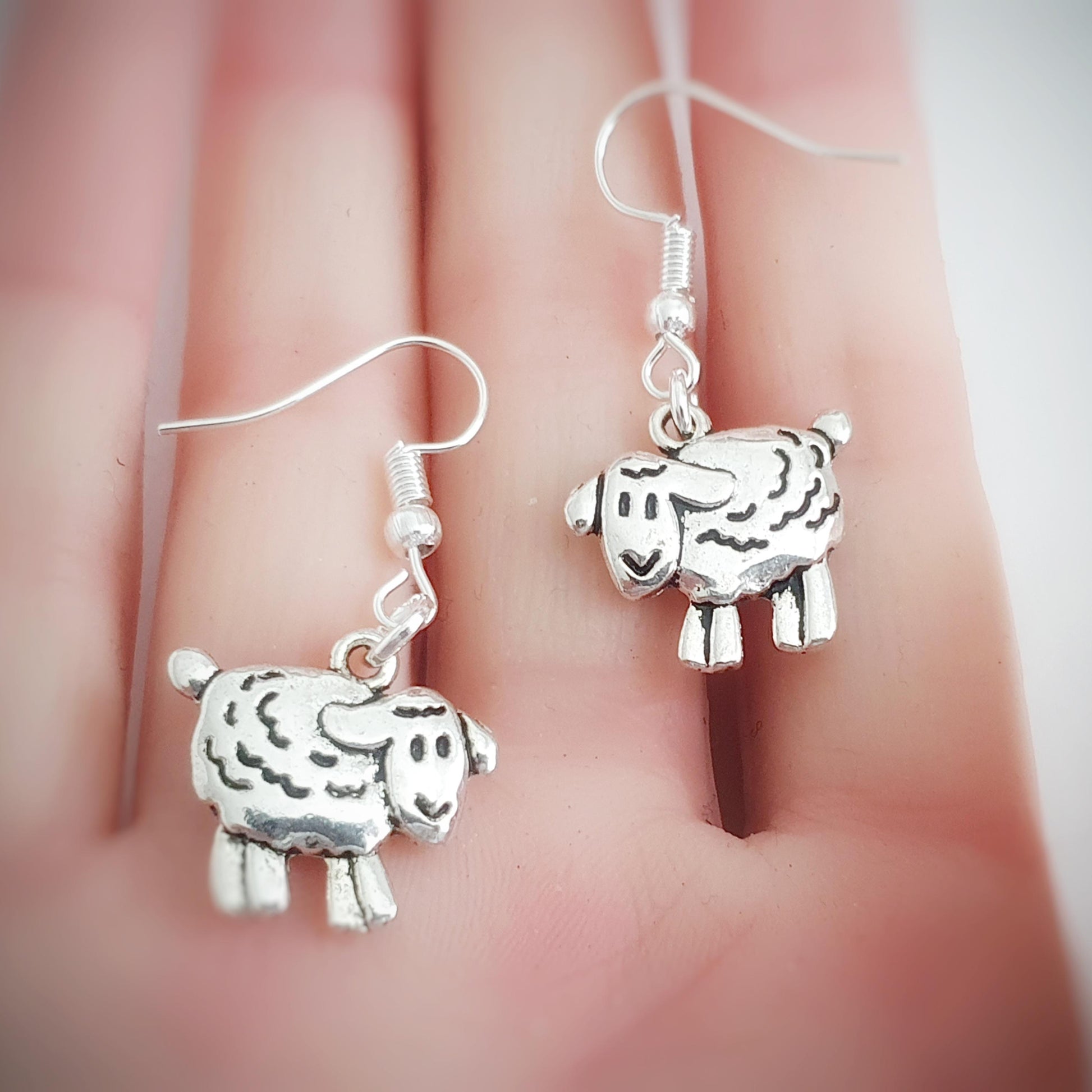 Silver sheep-shaped earrings on a hand with a blurred background